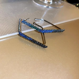 Macro view of U-shaped silver earrings with blue gradient crystals on glitter background