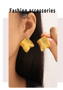 Detail of gold square earrings with irregular grid texture worn by a model