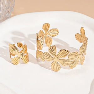 Detailed close-up of golden metal ginkgo leaf and flower open cuff bracelet and ring set