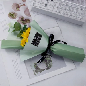 Detail of single artificial sunflower bouquet wrapped in green paper with a gift ribbon