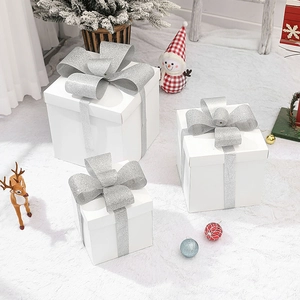 Three-piece set of white Christmas gift boxes with silver glitter bows on a white faux fur rug