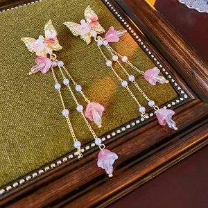 Detail von Schmetterlingsohrringen mit rosa Blumen und Perlen auf grünem Samt