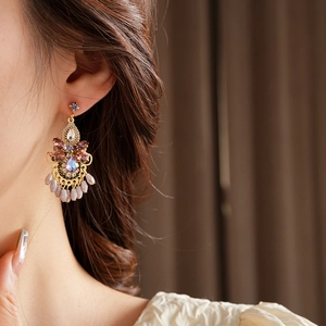 Close-up of luxury gold crystal earrings with purple tassel on a model side profile