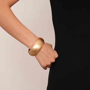 Detail of wide matte gold adjustable cuff bracelet worn on female wrist for styling