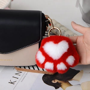 Detail of soft red and white faux fur cat paw keychain with gold ring on a bag