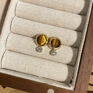 Close-up of gold earrings with brown round stones and clear gems in a jewelry box