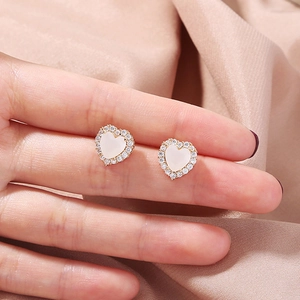 Close-up of heart-shaped gold stud earring with white stone and zircon on a fingertip