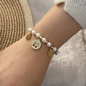 Detail eines Perlenarmbandes mit goldenen Lebensbaum-Anhängern am Handgelenk