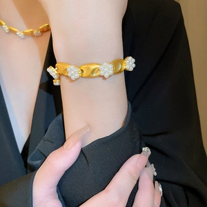 Vintage gold metal bangle with white pearl flower clusters on a black suit background