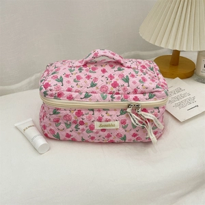 Pink floral quilted makeup bag with handle on bed featuring large capacity storage