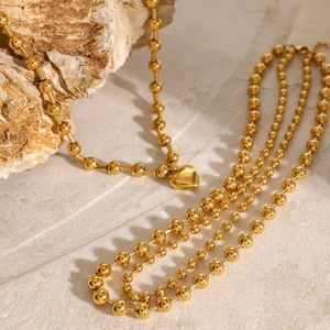 Polished 18k gold heart pendant necklace with layered bead chains on stone background