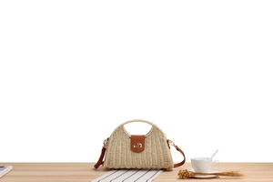 Detail of paper rope woven crossbody bag with brown leather handles on wooden table