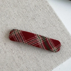 Detailed texture of red plaid fabric hair clip on neutral linen background