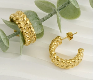 Detail shot of twisted gold C-shape hoop earrings on a marble surface with eucalyptus