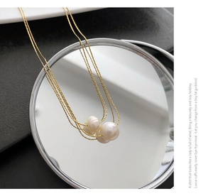 Detail of elegant gold layered chain necklace featuring three natural baroque pearls on a mirror