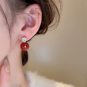 Close-up of elegant gold earrings with clear zircon and deep red beads on model