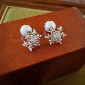 Macro shot of silver snowflake earrings with cubic zirconia and pearls on brown leather box