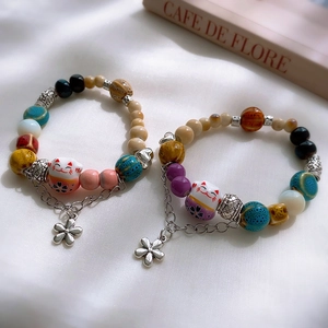 Detail of colorful ceramic lucky cat bracelets with floral charms and beads on white silk
