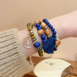 Detail of layered bohemian sandalwood bead bracelets with tree of life charm and blue tassel
