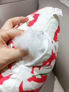 Detail of leaf pillow zipper closure showing white fiber filling and red printed fabric