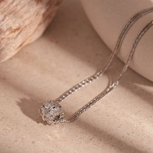 Dettaglio di una collana multistrato argentata con pendente cilindrico e zirconi trasparenti