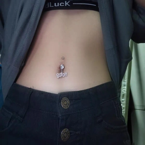 Silver belly button ring with zircon accents and a Bitch word pendant on a model