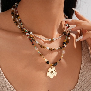 Detail of layered tiger eye beaded necklace with a golden floral pendant on model