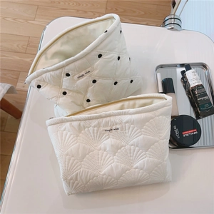 Detail view of white quilted cosmetic bags with wave and dot embroidery textures