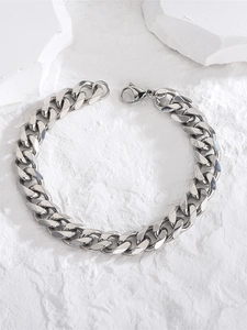 Detailed view of silver stainless steel Cuban link bracelet on a white textured stone surface