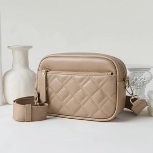 Beige quilted crossbody camera bag with gold zipper and wide fabric shoulder strap