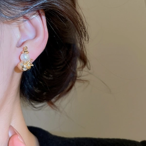 Close-up of hulu shaped earrings with white pearl and sparkling crystals on model ear