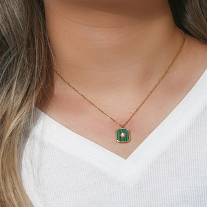 Detailed view of a gold necklace featuring a green rectangular starburst pendant on a model