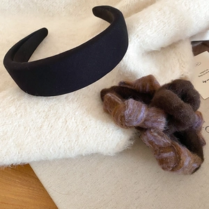 Detail of a black fabric headband and fuzzy brown-purple scrunchie set on soft textile