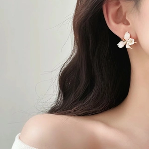Detailed side view of a delicate white flower and butterfly earring on a model's ear
