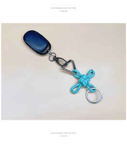 Detail of teal Chinese knot keychain with silver metal lobster clasp on yellow background