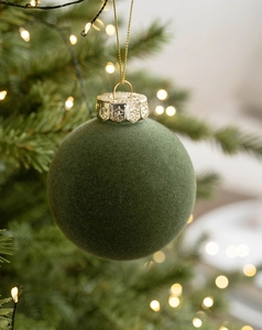 Close-up of green flocked velvet Christmas ball with gold hanging loop and festive bokeh