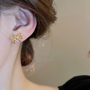 Close-up of a delicate gold bow stud earring worn on ear with polished metallic finish