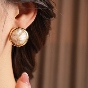 Gros plan d'une boucle d'oreille ronde dorée à texture perlée sur le mannequin