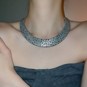 Close-up of a wide silver choker with intricate woven texture on a fashion model
