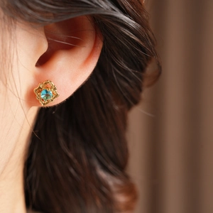 Close-up of vintage gold hollow-out earrings with blue crystal on female ear