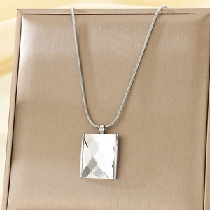 Close-up of a square white crystal pendant hanging on a silver snake chain over silk