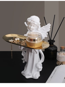 Detail of white resin angel statue holding a gold metal tray for jewelry storage