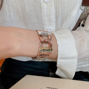Close-up of a tricolor metal charm bracelet with DREAM and LOVE engraved plates