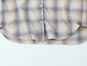 Dettaglio camicia a quadri con orlo curvo, trama in cotone e lino e piccoli bottoni bianchi