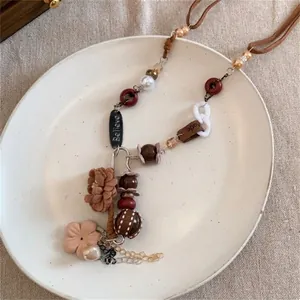Détail du collier bohème avec fleur en tissu et breloques gravées sur lin beige