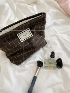 Detail view of coffee plaid tweed makeup bag with logo label on white linen background
