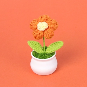 Detail einer handgehäkelten orangefarbenen Blume im weißen Keramiktopf auf orangefarbenem Grund