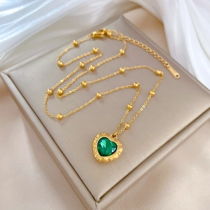 Detail of green heart pendant on golden titanium steel chain over satin background