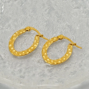 Detail of gold oval hoop earrings with hammered texture on a textured glass tray