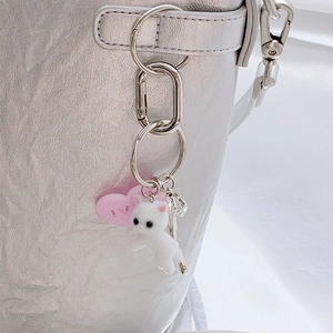 Cute white plush cat keychain with pink heart tag hanging on a silver bag accessory